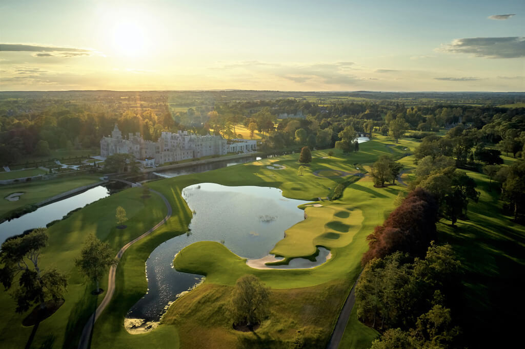 aerial shot of adare manor with lake and castle and wooded area