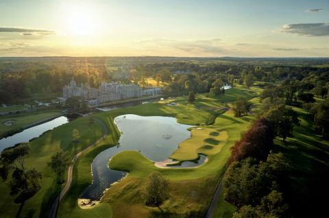 aerial shot of adare manor with lake and castle and wooded area