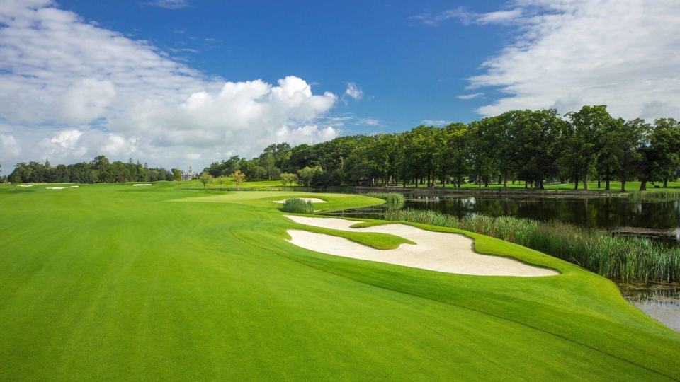 View of golf course with cloudy blue skies and a bunker on the right hand side of the image