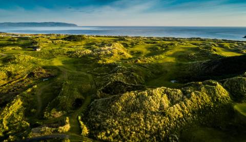 hilly green golf course with sea in the background