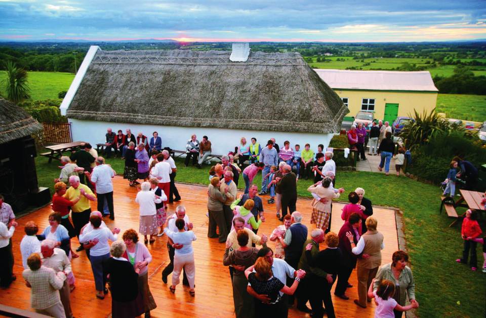 group of people dancing on a wooden floor near a thatched cottage