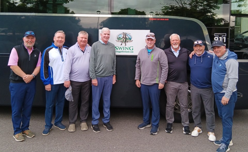 8 middle-aged men standing in front of a swing golf tour bus wearing golf gear.