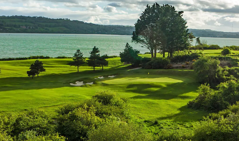 Golf course with trees, mountains and water in the background.
