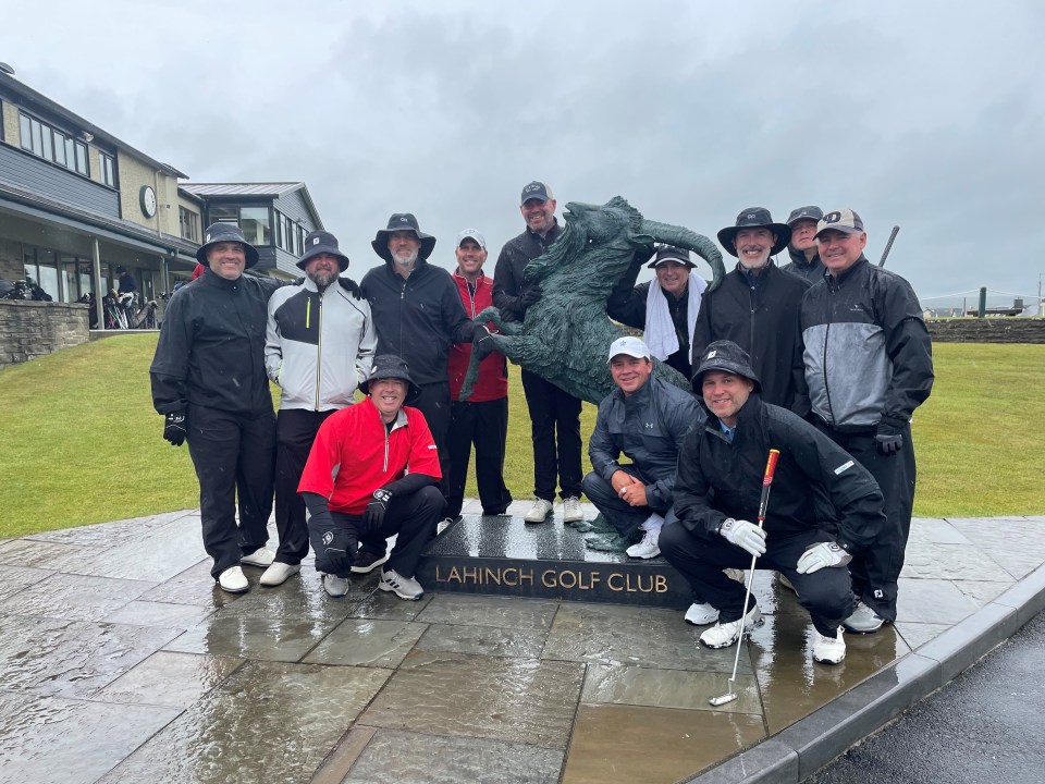 Group of men wearing golfing rain gear surrounding a statue in the south of Ireland