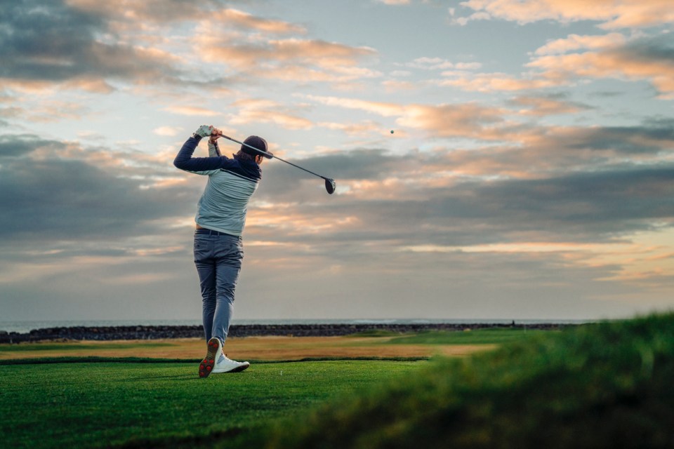 Male athlete teeing off at golf course during sunset