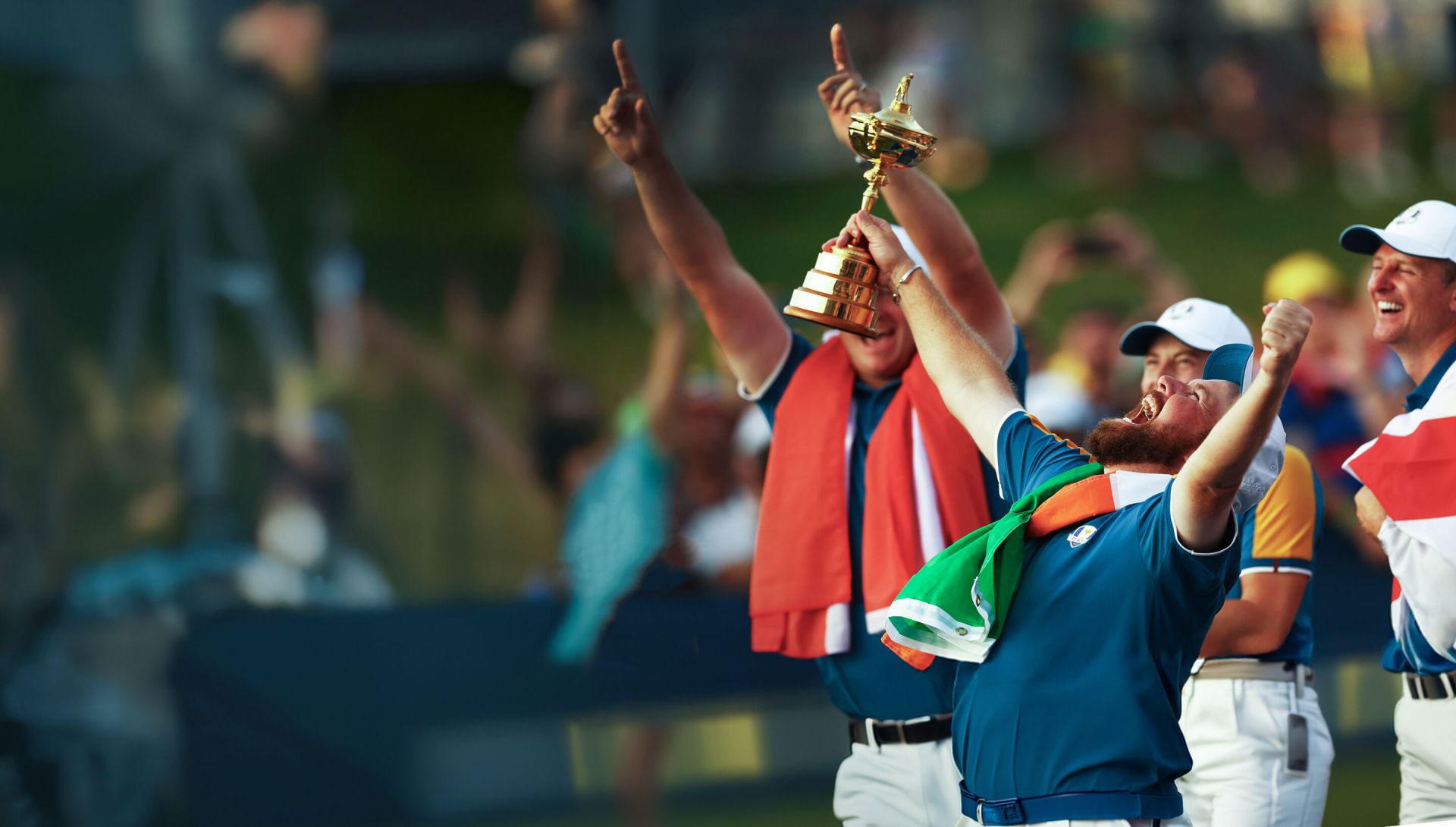 Celebrating golfer holding the Ryder Cup with fans cheering in the background