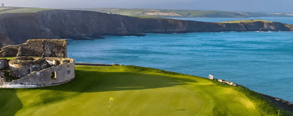 Golf course beside the sea, with cliffs and farmland in the background, and old ruins.